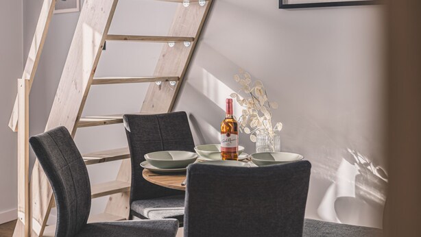 Comedor con techo estilo loft, una mesa con platos, una botella y ramas decorativas.