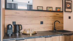 Una cocina moderna con protector de salpicadero de madera, encimera negra, cafetera, hervidor y una bandeja con vasos.
