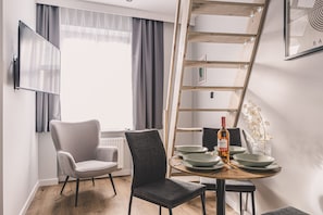 Et moderne spiseområde med en træstige, to stole, et bord dækket med tallerkener og en flaske, samt et vindue med gardiner.