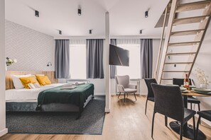 Moderni hotellihuone, jossa on sänky, työpöytä tuolilla, televisio ja puinen tikapuu.