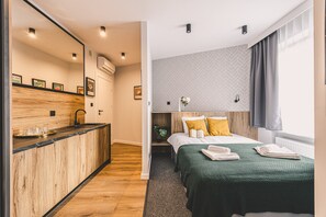Hotellihuone, jossa on puinen baaritiski, vihreillä tekstiileillä varustettu sänky ja ikkuna, jossa on verhot.