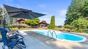 Una piscina con zona de terraza, sillas de descanso y una sombrilla.