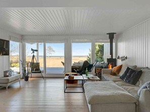 Ein großzügiges Wohnzimmer mit einem großen Fenster mit Blick auf einen Strand, einem Kamin und einem auf einem Stativ stehenden Teleskop.