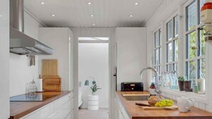 A modern kitchen with white cabinetry, a wooden countertop, a built-in stove, and a window with a view of greenery. - 5 Star Holiday Home in Hillerod (Hillerod)