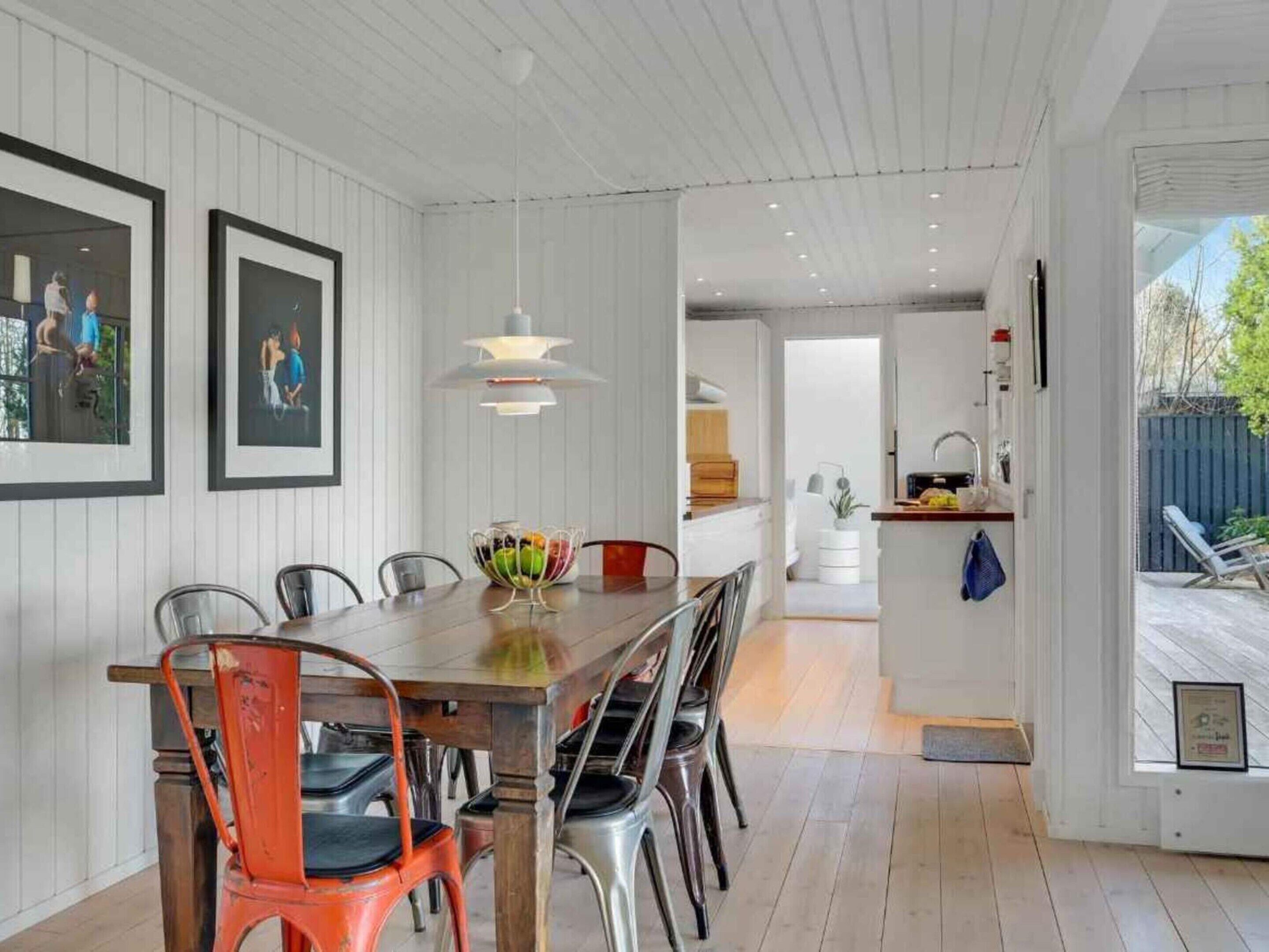 A modern kitchen with white cabinetry, a dining area with a wooden table and metal chairs, and a view of the backyard through an open door.