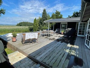 A wooden deck with outdoor furniture, a covered seating area, and a view of a green landscape. - 5 Star Holiday Home in Hillerod (Hillerod)