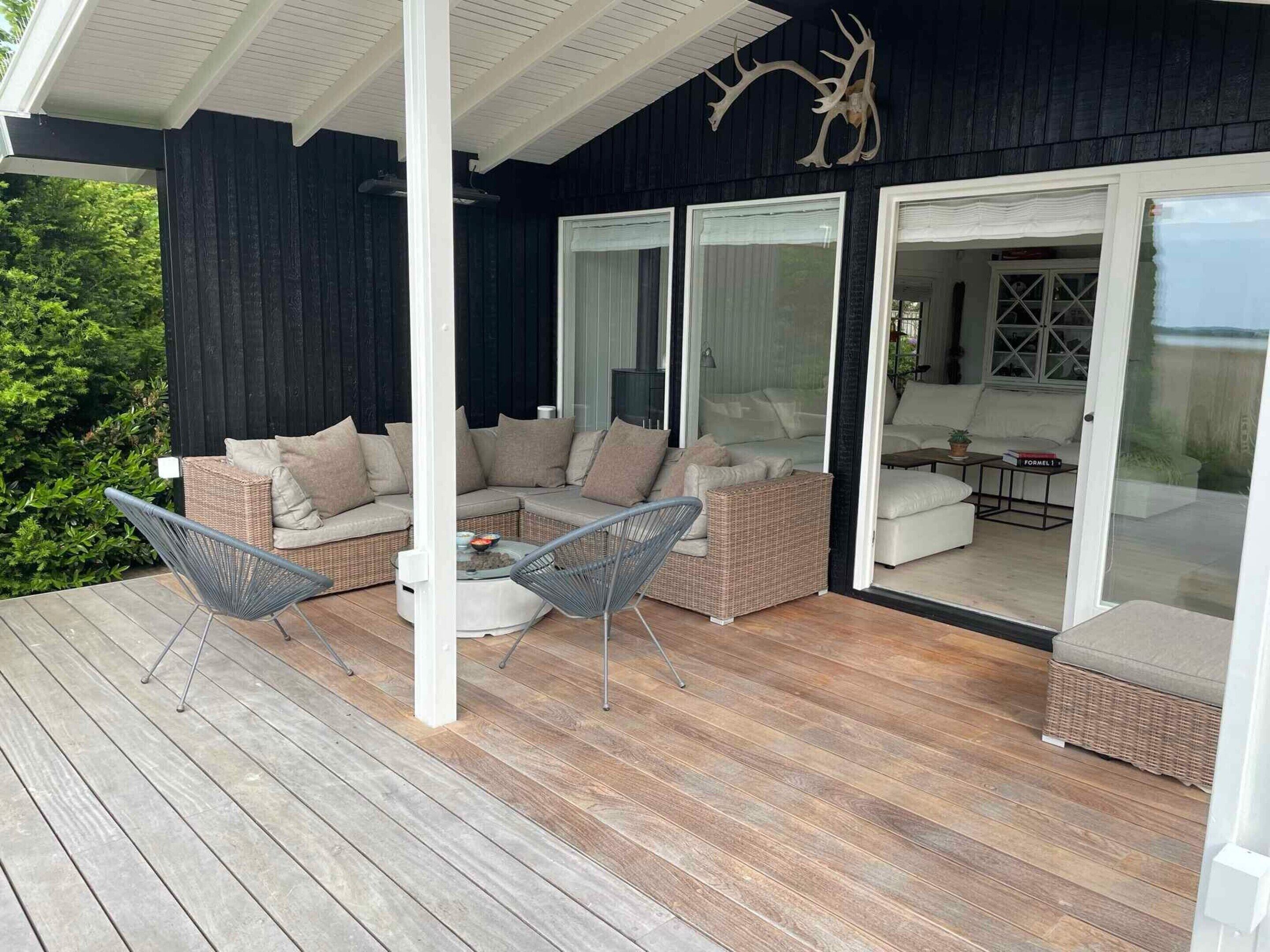 Un espace extérieur aménagé, abrité et doté de mobilier en osier, avec une porte vitrée donnant accès à un espace intérieur.
