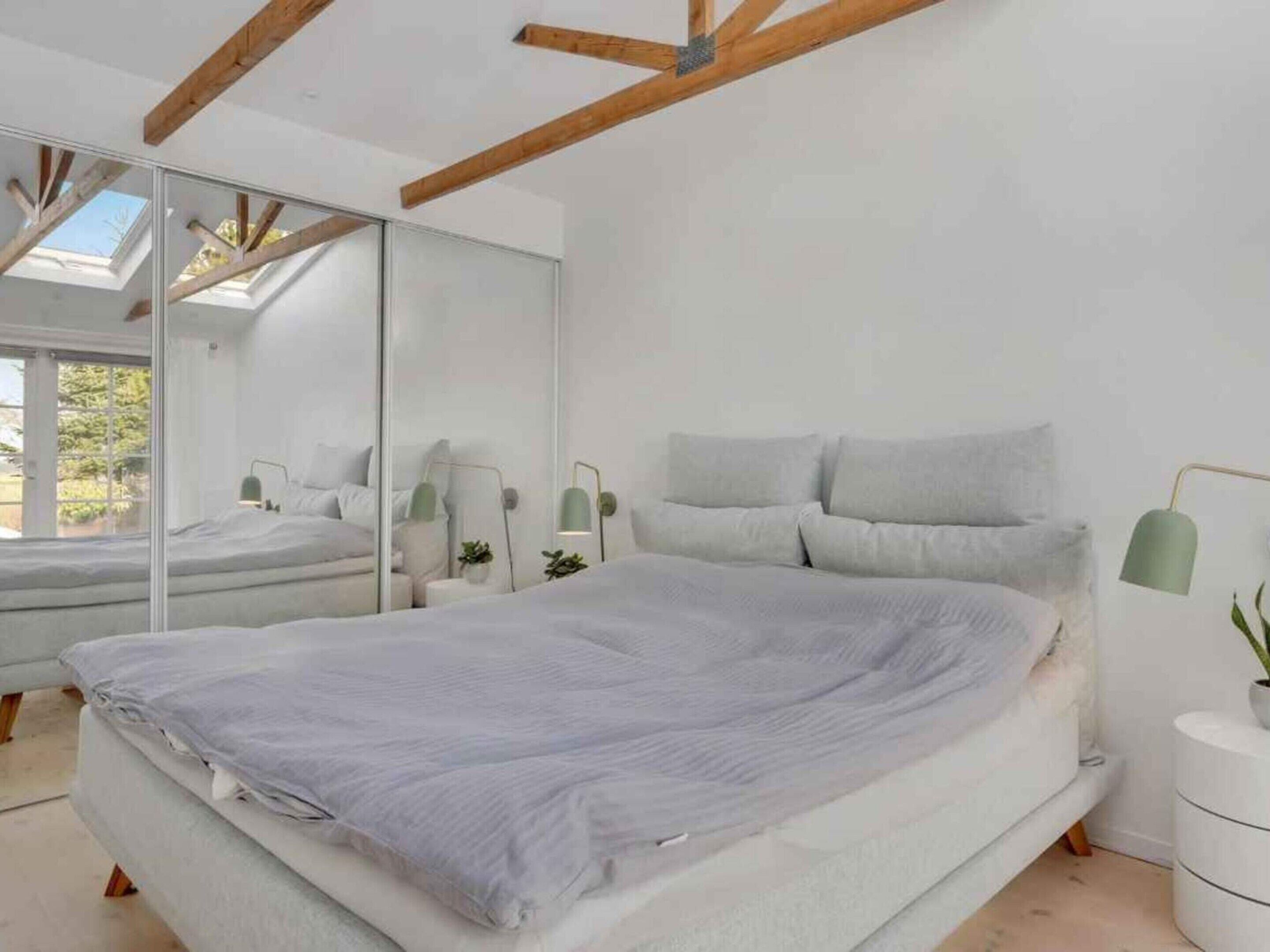 A modern bedroom with a large bed, a mirror, bedside tables, and a skylight.