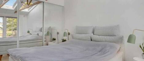 A modern bedroom with a large bed, a mirror, bedside tables, and a skylight.