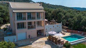 Une maison à deux étages avec une piscine, un espace salon extérieur et une vue sur les collines environnantes.