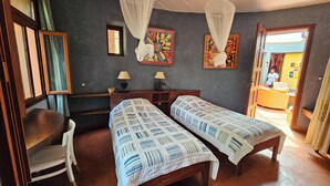 A room with two beds, a desk, and a chair. There are two paintings on the wall and a window with curtains. - VILLA BOUTANGA (Bangoulap)