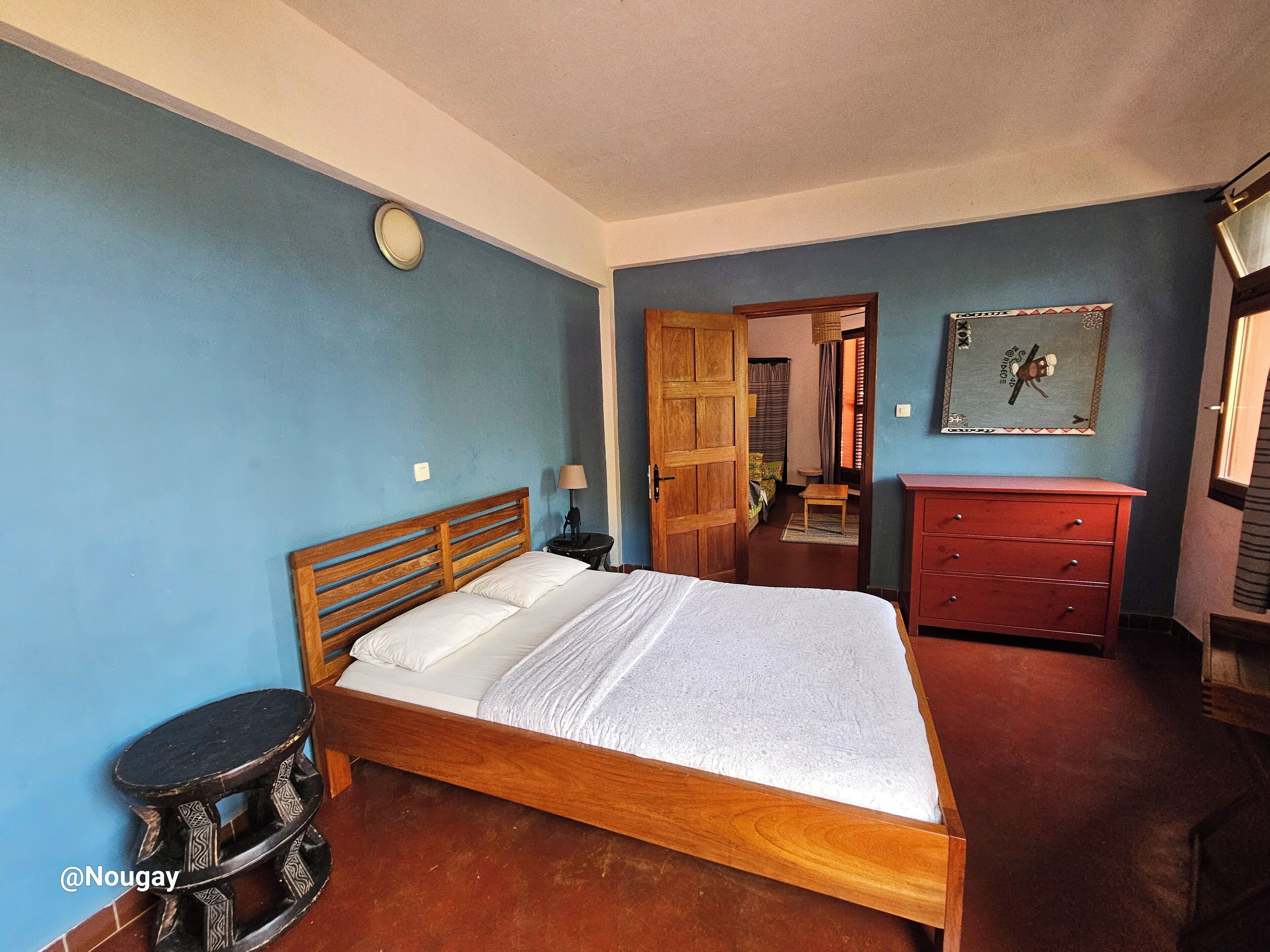 A bedroom with a wooden bed, a red dresser, a small stool, and a wall clock.