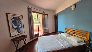 A bedroom with a bed, a wooden headboard, a nightstand, a framed picture on the wall, and a window with curtains. - VILLA BOUTANGA (Bangoulap)