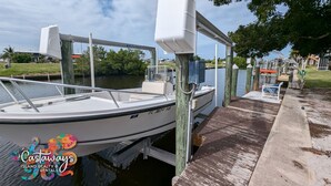 Un barco amarrado en un puerto deportivo, con un muelle de madera, una pequeña silla y un flotador salvavidas.
