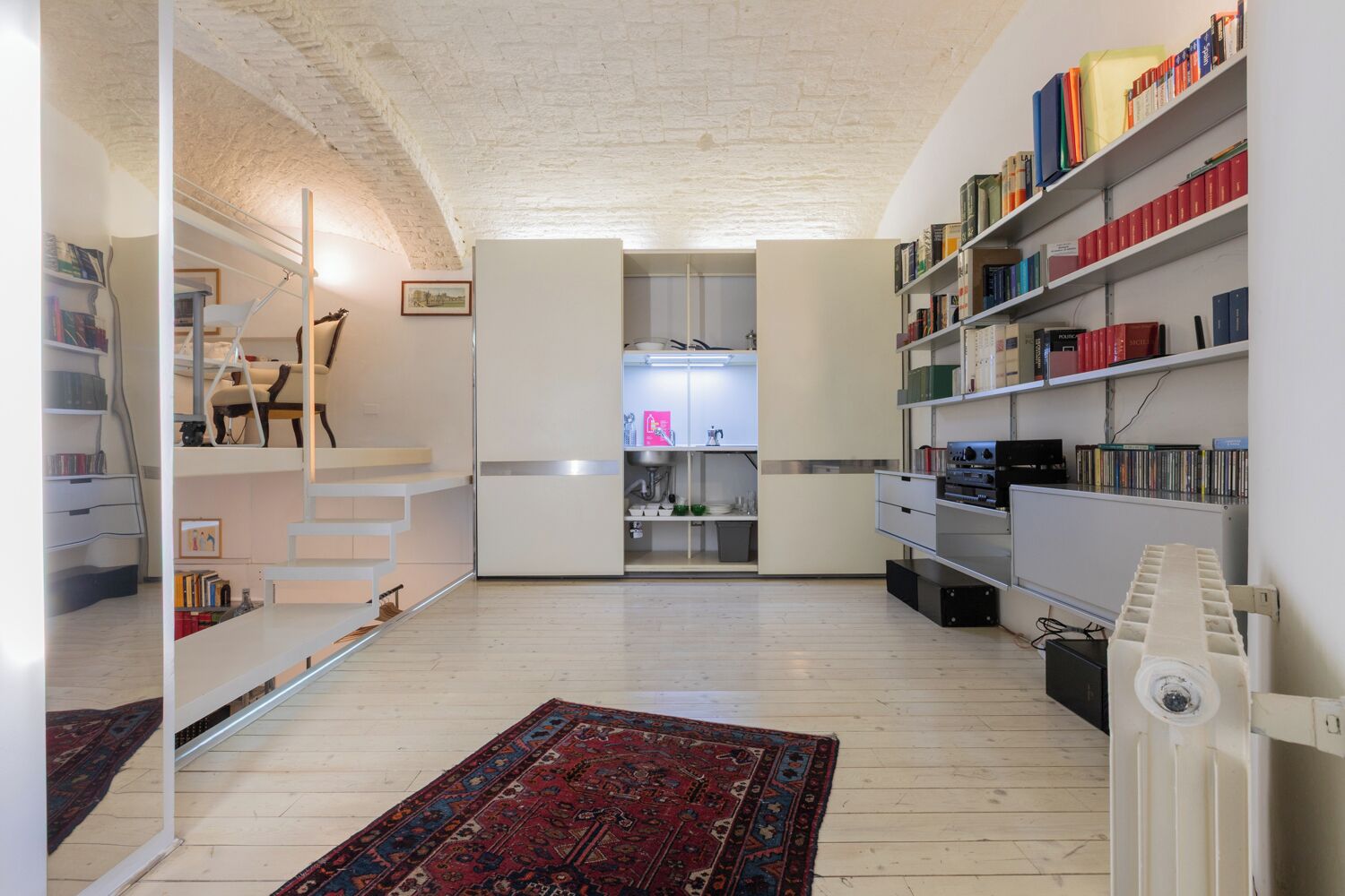 Un interior moderno con cama tipo loft, estanterías empotradas, zona de cocina y alfombra estampada.
