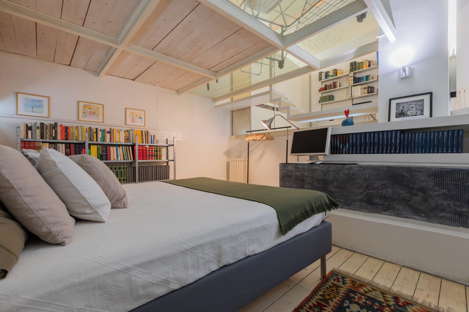 A bedroom with a bed, a bookshelf, a desk with a computer, and a skylight.
