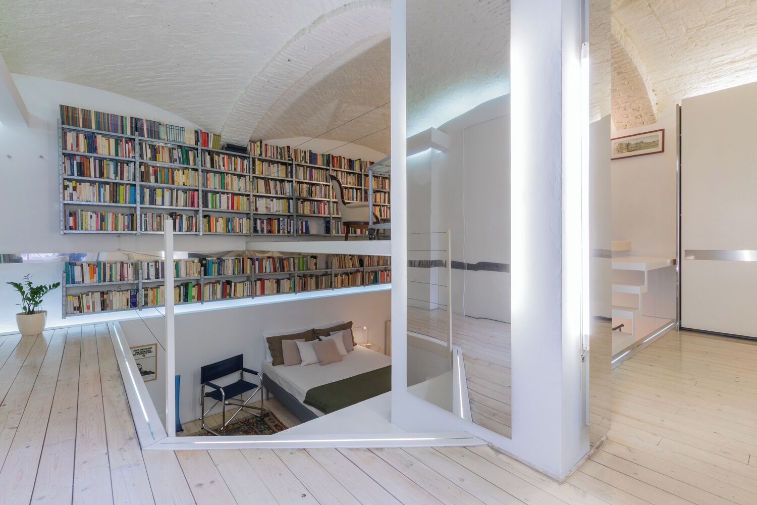 A modern interior with a multi-level bookshelf, a bed, and a small seating area.