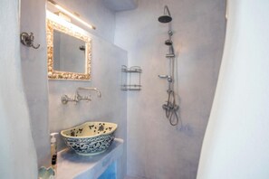 A bathroom with a large mirror, a sink with a decorative bowl, and a shower area. - Villa Pisti by Apleton Villas Paros (Paros)