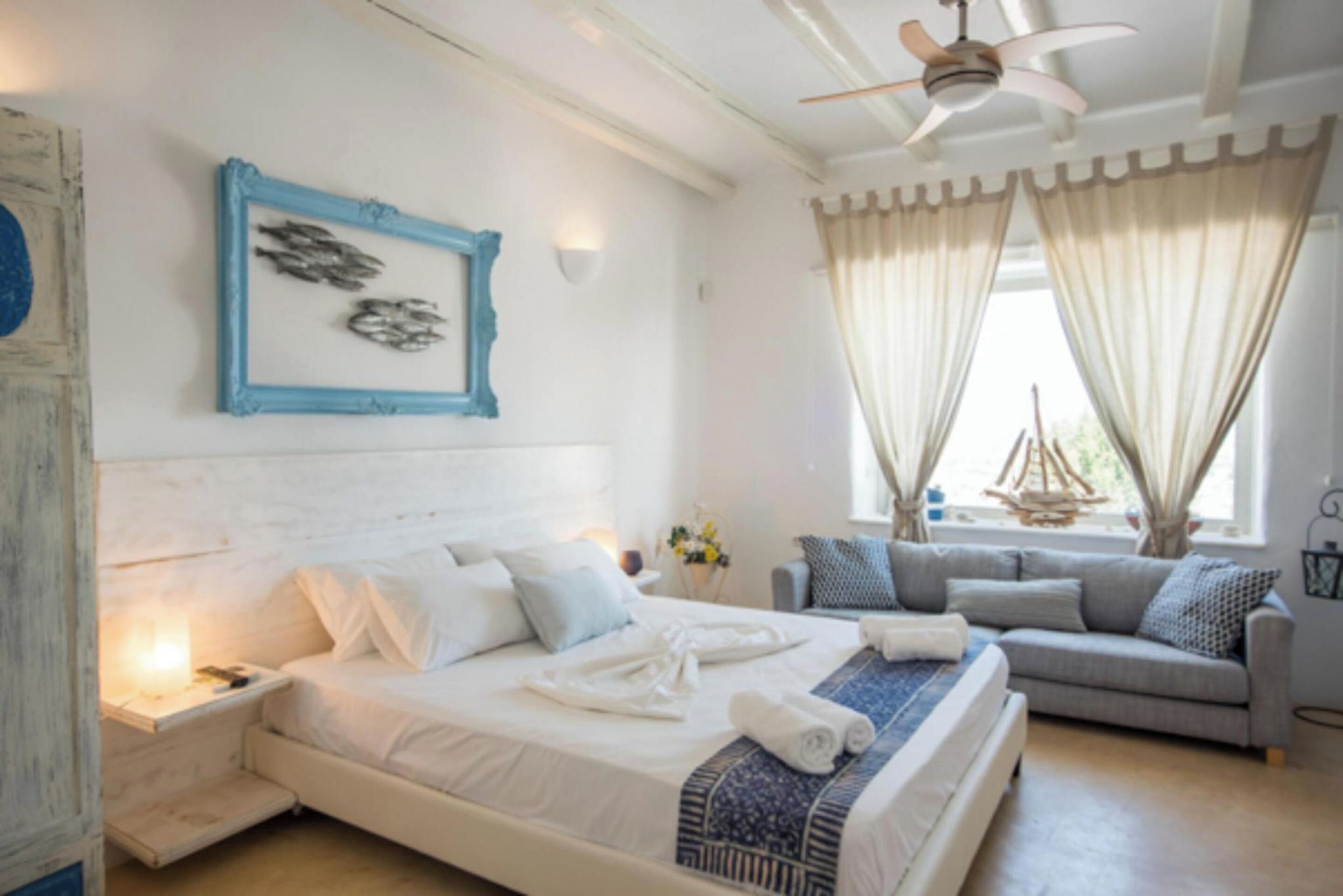 A bedroom with a bed, a nightstand, a sofa, and a ceiling fan.