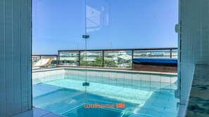 Une piscine sur le toit, avec une eau d’un bleu cristallin, entourée d’une barrière de verre et d’une terrasse en bois.