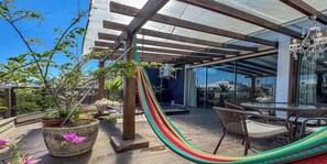 Une terrasse sur le toit aménagée avec un hamac, des meubles en osier, des plantes en pot et un espace repas fermé par des parois de verre.