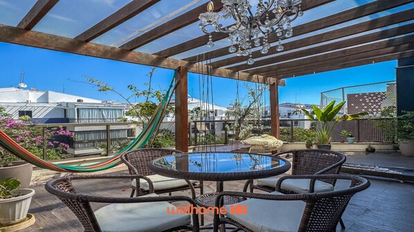 Une terrasse sur le toit aménagée avec des meubles en osier, une table en verre et un hamac.
