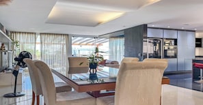 A modern living room with a glass coffee table, beige sofas, and a dining area with a glass table.