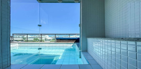 A clear view of a swimming pool with a glass barrier, tiled walls, and a view of buildings in the background.