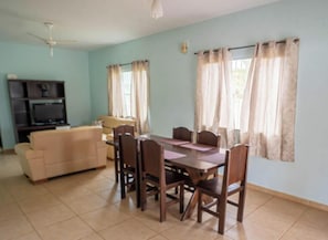 A dining area with a table and chairs, a sofa, a TV stand, and curtains on the windows.