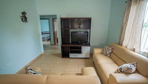 A living room with a sofa set, a TV stand, and a door leading to another room.