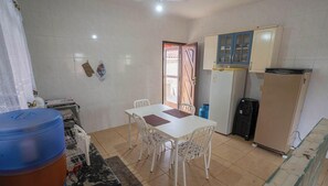 Uma cozinha com mesa branca, cadeiras, geladeira e um bebedouro azul.