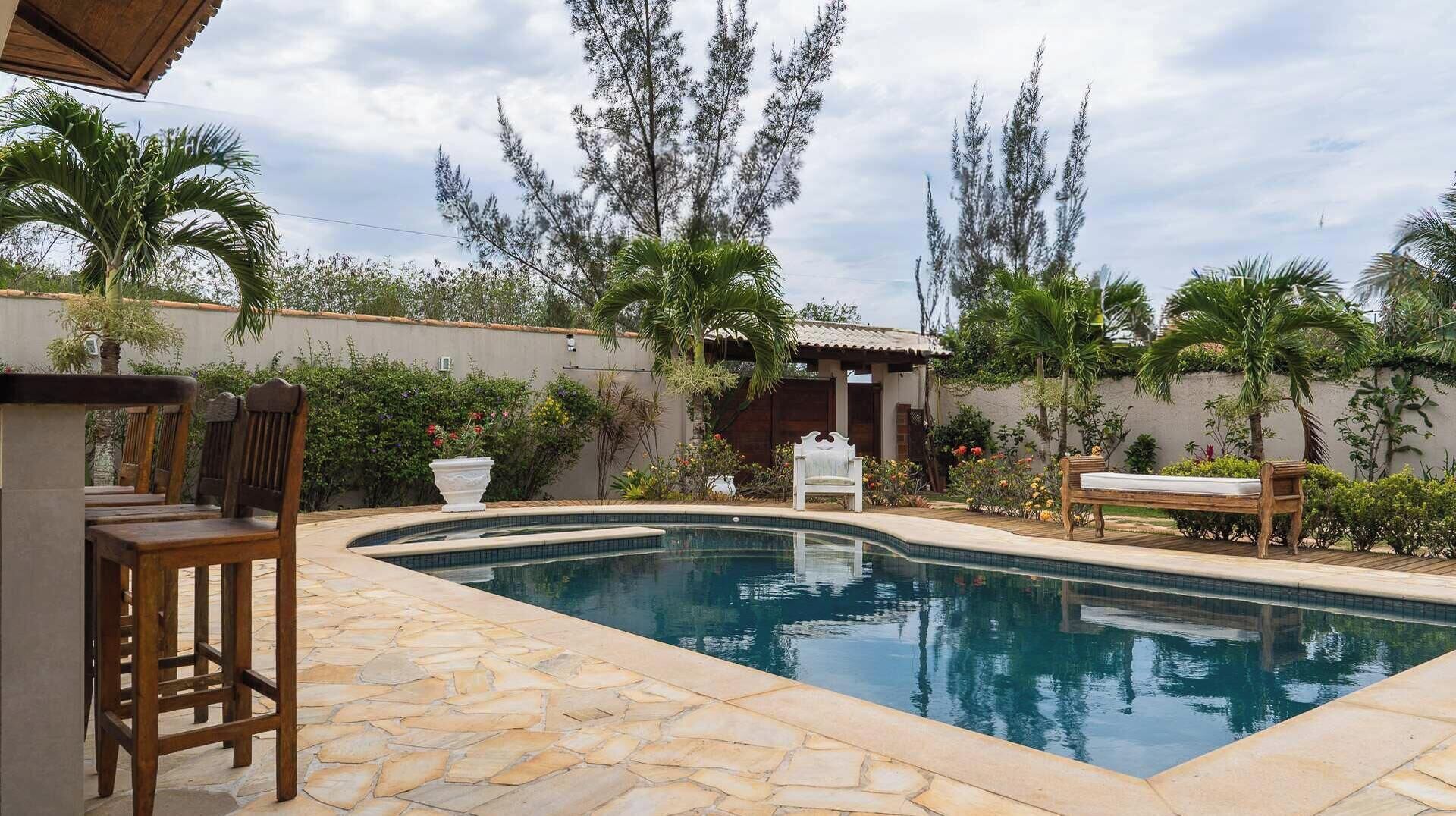 Una piscina con baldosas de piedra, sillas de madera y un banco.