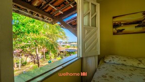 Ein Zimmer mit einem Bett, einem Fenster mit geöffneter Tür, einem Gemälde an der Wand und Blick auf einen Garten mit Palmen.