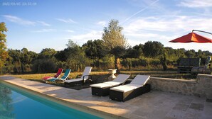 A poolside area with lounge chairs and a red umbrella.