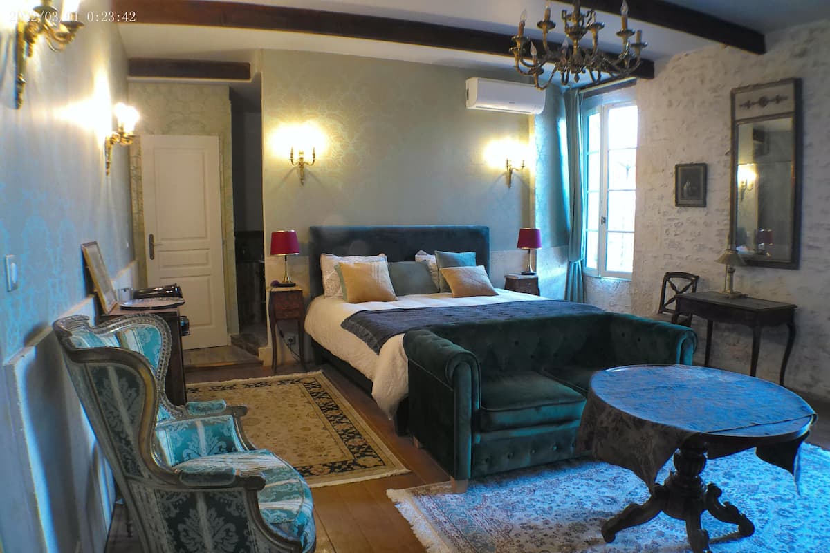 A bedroom with a large bed, a sitting area with a table, and a chandelier.