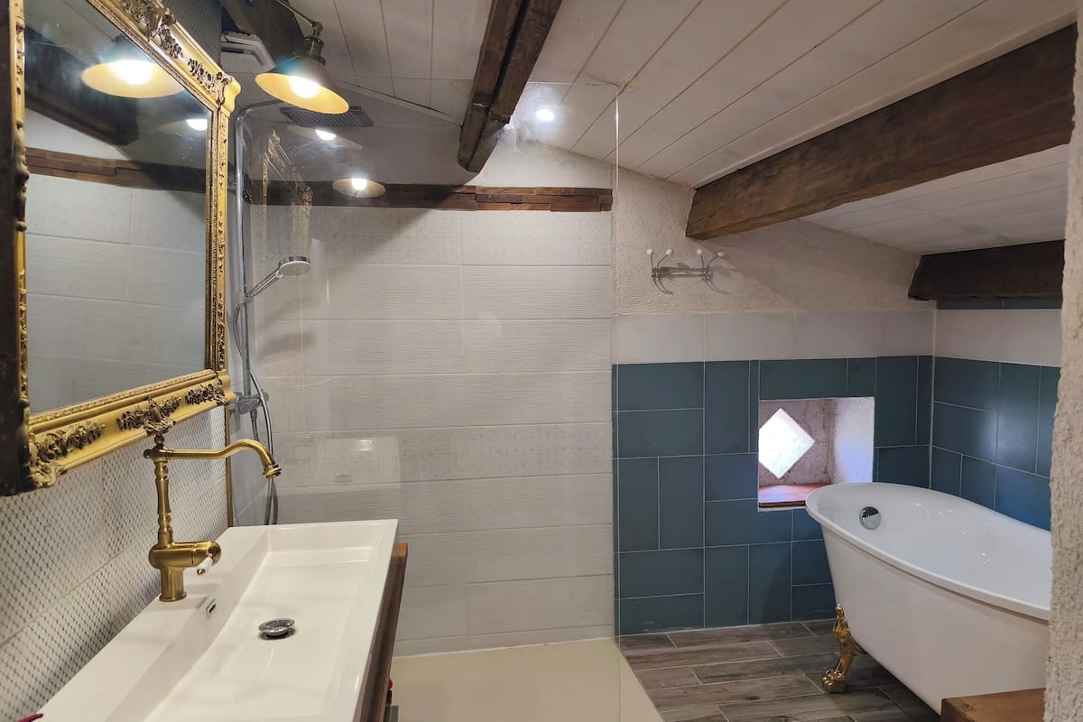 A bathroom with a white sink, gold faucets, a large mirror, a freestanding bathtub, and a shower with a gold faucet.