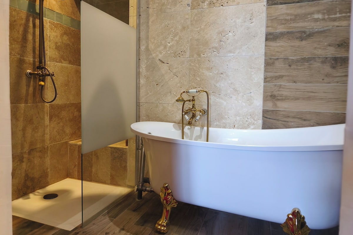 A modern bathroom with a freestanding bathtub, a glass-enclosed shower, and a marble-tiled wall.