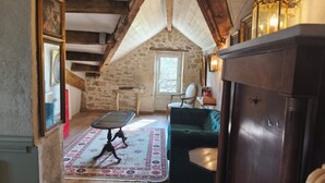 A cozy attic room with a wooden ceiling, a green sofa, a small table, and a decorative mirror.
