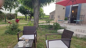 An outdoor seating area with wicker chairs and a glass table, a red umbrella, and a stone building in the background.