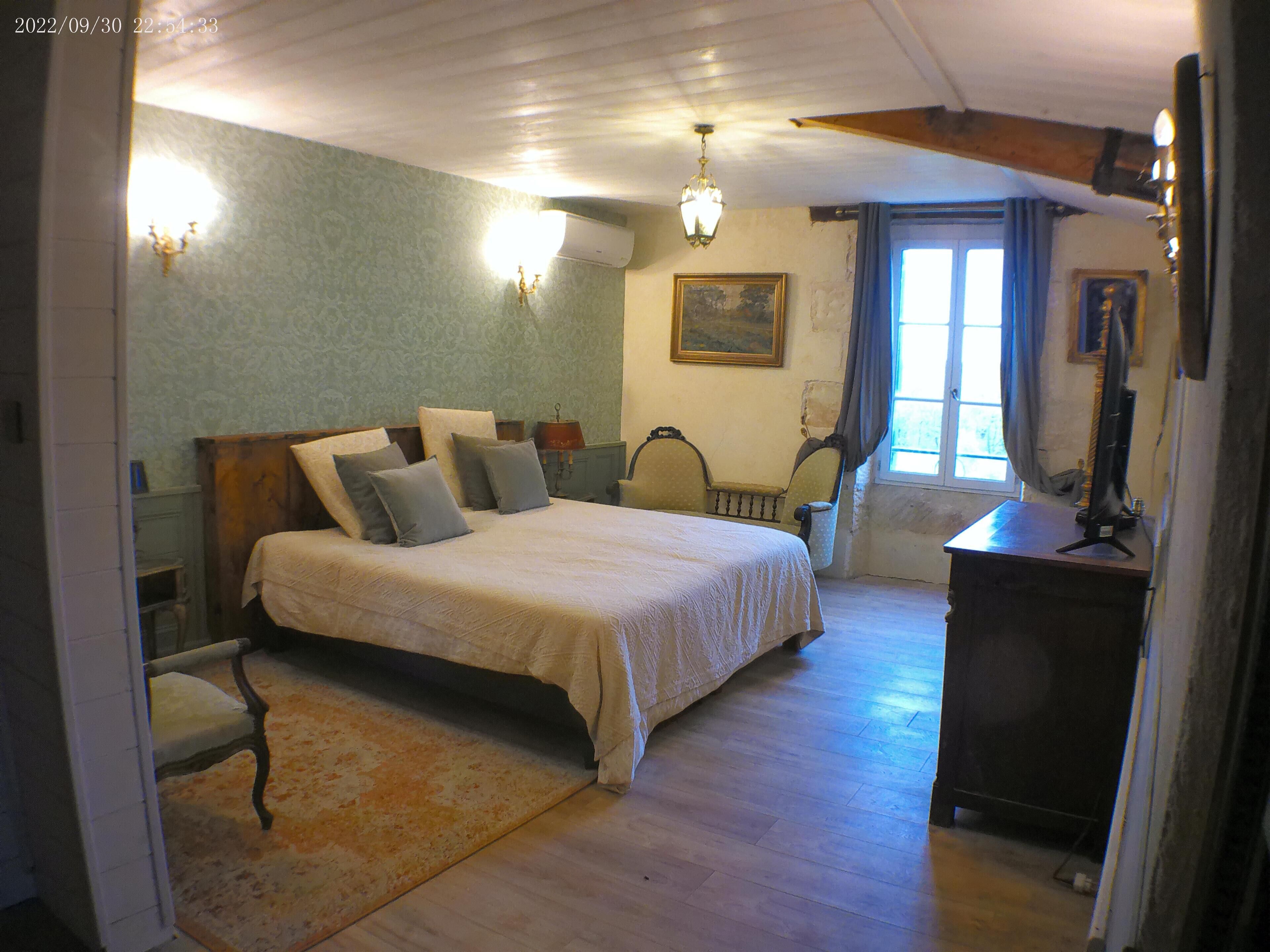 A bedroom with a large bed, a wooden dresser, a desk, a chair, and a window with curtains.