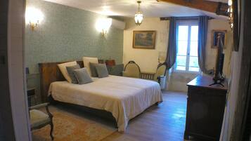 A bedroom with a large bed, a wooden dresser, a desk, a chair, and a window with curtains.