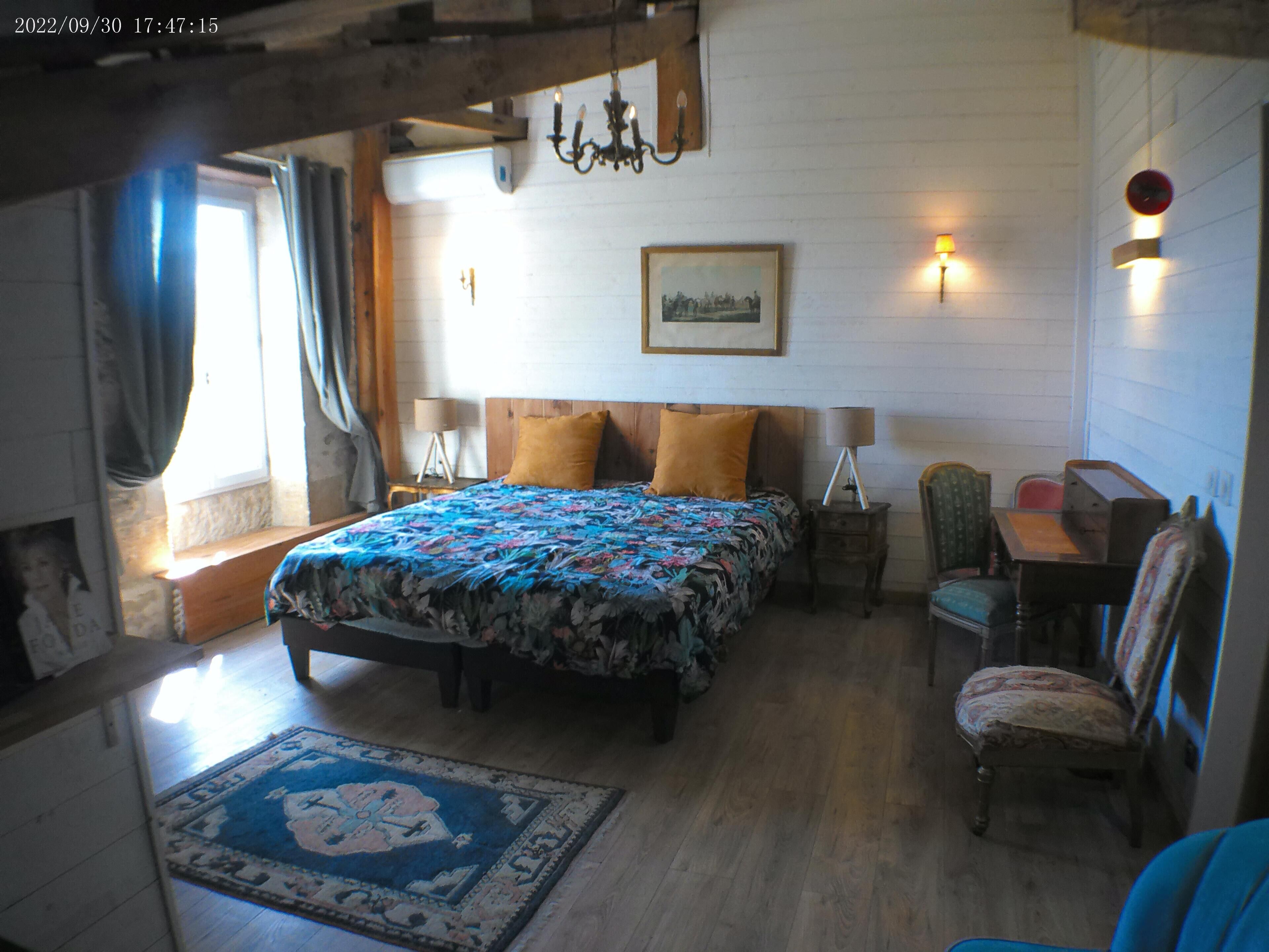 Ein Schlafzimmer mit einem hölzernen Bett, einem Nachttisch, einem Stuhl, einem Schreibtisch und einer Wandlampe.