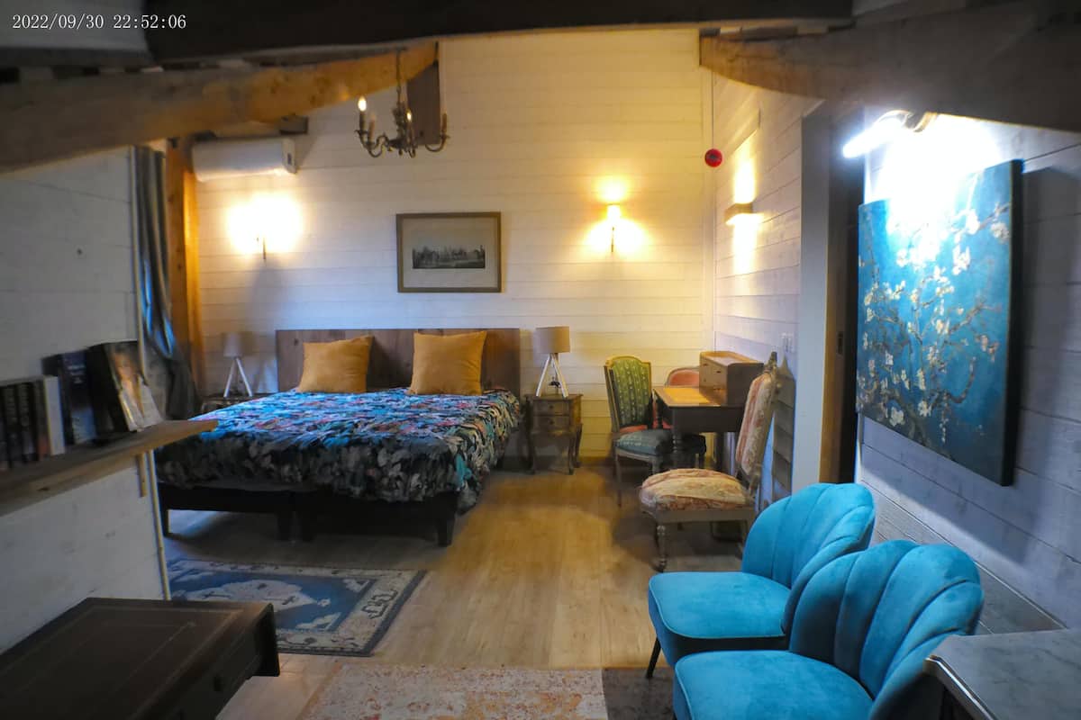 A cozy room with a bed, a desk, two chairs, a lamp, and a painting on the wall.