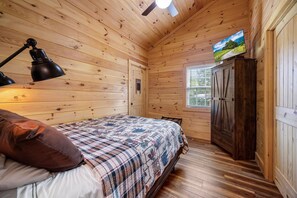 A wooden cabin room with a bed, a desk, a lamp, and a television on a wooden cabinet. - The Homestead 2 Bedroom Cabin (Cosby)