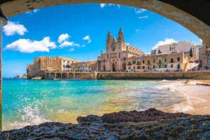 A coastal cityscape with a prominent cathedral and a rocky shoreline.