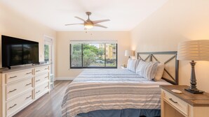A bedroom with a bed, a TV, a ceiling fan, a window with a view, and a nightstand with a lamp. - Santa Maria II #111 (Fort Myers Beach)