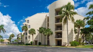 A multi-story hotel with a curved facade, palm trees, and a clear blue sky. - Santa Maria II #111 (Fort Myers Beach)