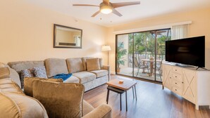 A modern living room with a sofa, a coffee table, a TV, and a ceiling fan. - Santa Maria II #111 (Fort Myers Beach)