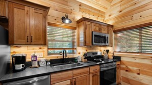 A modern kitchen with wooden cabinetry, stainless steel appliances, and a black countertop. - Cabin On A Hill 2 Bedroom Cabin (Cosby)