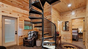 A wooden interior with a spiral staircase, a leather chair, a rug with a bear design, and a bed with a floral bedspread. - Cabin On A Hill 2 Bedroom Cabin (Cosby)